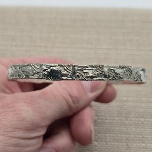 May include: A silver bangle bracelet with a textured design.