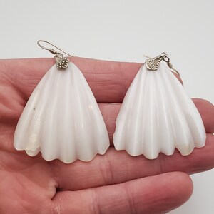 May include: A pair of white shell earrings with silver accents. The earrings are shaped like a fan and have a delicate, feminine look.