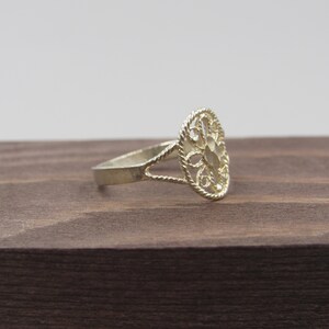May include: A silver filigree ring with a delicate, openwork design. The ring is oval-shaped and has a smooth, polished finish.