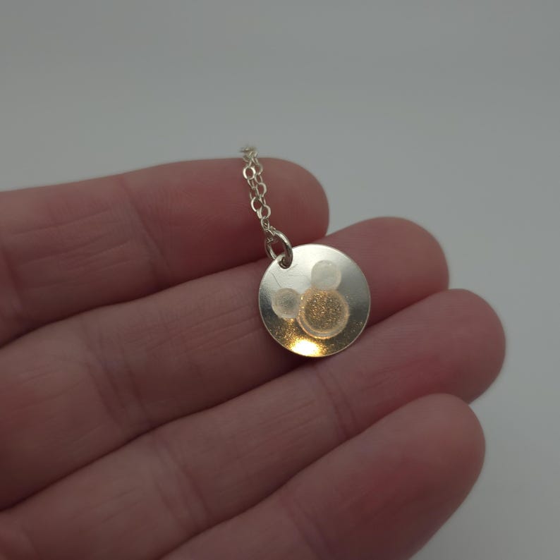 May include: A silver necklace with a round pendant featuring a Mickey Mouse silhouette.