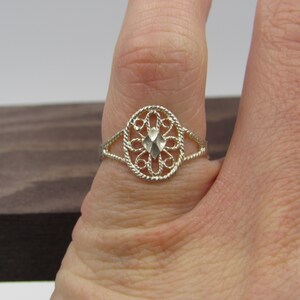 May include: A silver filigree ring with a diamond-shaped center stone. The ring is on a finger.