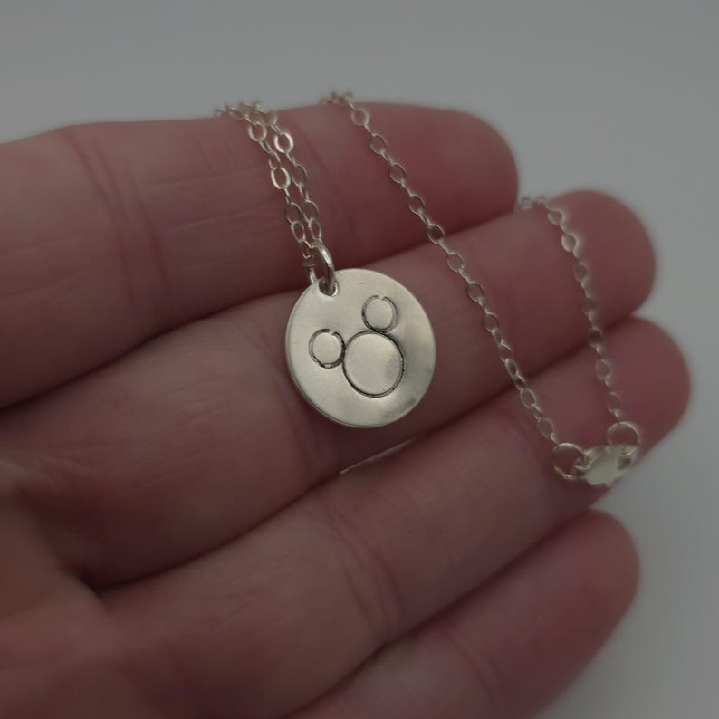 May include: A silver necklace with a round pendant featuring a Mickey Mouse silhouette.
