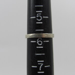 May include: A silver ring sized 6 on a black ruler with markings for sizes 5, 6, and 7.