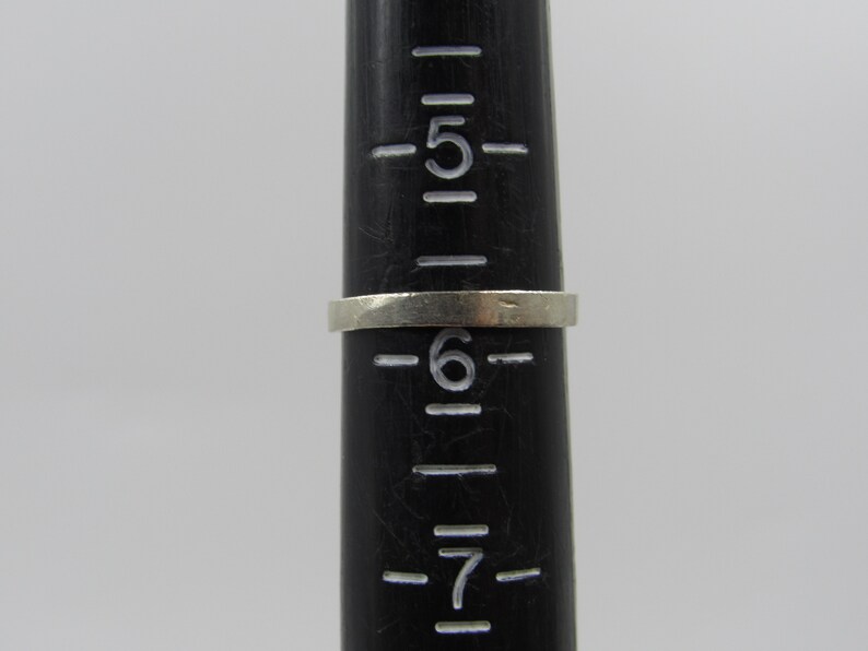 May include: A silver ring sized 6 on a black ruler with markings for sizes 5, 6, and 7.