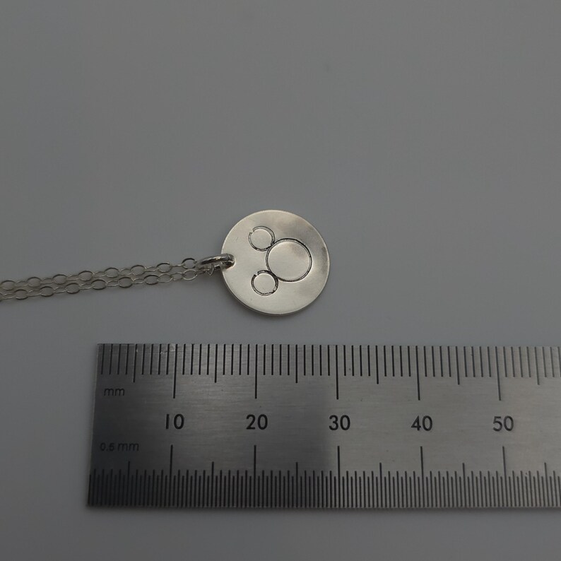 May include: A silver necklace with a round pendant featuring a three-circle design. The pendant is approximately 2 cm in diameter.