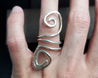 May include: A silver ring with a unique, abstract design. The ring is made of twisted wire and has a hammered finish.