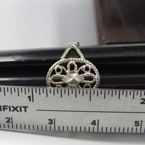 May include: A silver filigree ring with a diamond-shaped center piece. The ring is measured against a ruler, showing it is approximately 1 inch in diameter.
