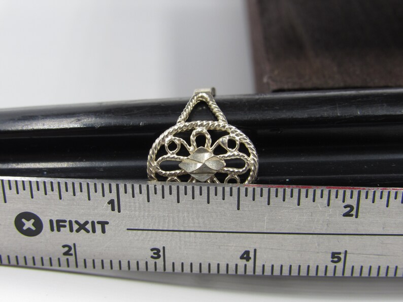May include: A silver filigree ring with a diamond-shaped center piece. The ring is measured against a ruler, showing it is approximately 1 inch in diameter.