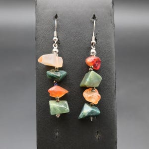 May include: A pair of dangle earrings featuring silver-toned hooks and a vertical arrangement of four irregular, tumbled gemstone beads in shades of orange, peach, and green, separated by small metallic spacer beads on each earring strand.