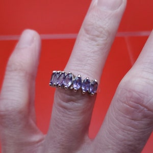 May include: A silver ring with a row of purple marquise-shaped gemstones.