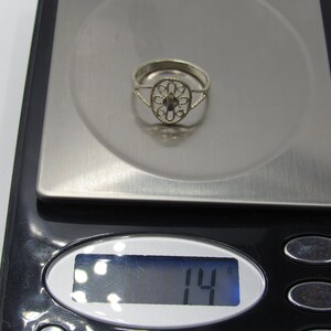 May include: A silver ring with a delicate filigree design, weighing 14 grams, displayed on a digital scale.