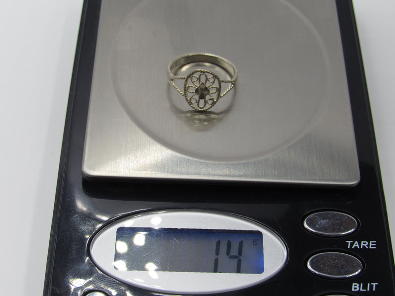 May include: A silver ring with a delicate filigree design, weighing 14 grams, displayed on a digital scale.