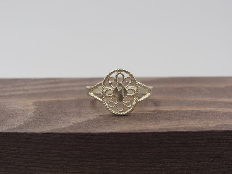 May include: A silver filigree ring with a delicate, intricate design. The ring is oval-shaped and has a floral pattern.