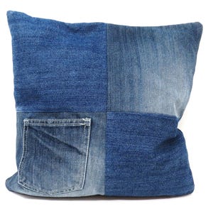 Puede incluir: Una almohada de mezclilla azul con un diseño de patchwork. La almohada tiene un bolsillo grande en la parte delantera.