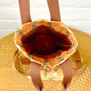 Op de afbeelding: Een bruine canvas draagtas met een bloemenpatroon. De tas heeft twee bruine hengsels en een ritssluiting.