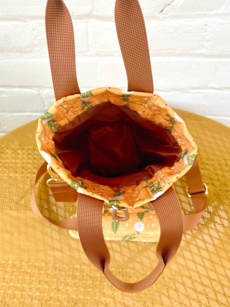 Op de afbeelding: Een bruine canvas draagtas met een bloemenpatroon. De tas heeft twee bruine hengsels en een ritssluiting.