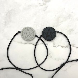 May include: Two black string bracelets with a pentagram charm. One charm is black and the other is gray.