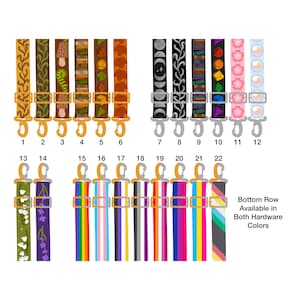 Puede incluir: Veintidós correas de tela ajustables con clips metálicos, numeradas del 1 al 22. Los diseños incluyen patrones botánicos, celestiales, de libros, dados de juego y banderas del orgullo. Texto a la derecha: Bottom Row Available in Both Hardware Colors.