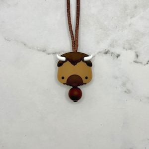 May include: A brown and white silicone necklace with a bison head charm and a brown wooden bead.