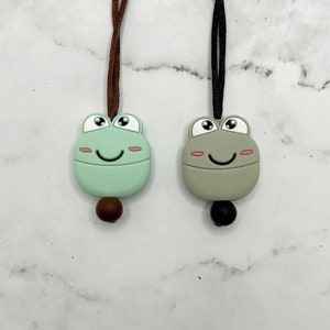 May include: Two frog-shaped silicone timer necklaces, one green and one gray, with brown and black cords. Each timer has a face with large eyes, a smile, and blush marks. The timers have a 60-second countdown scale.