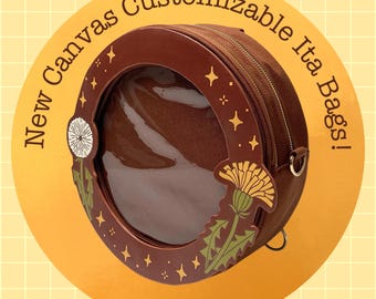 May include: A round brown canvas ita bag featuring a clear circular window on the front, surrounded by a dark brown frame decorated with dandelion illustrations and small star motifs. The text New Canvas Customizable Ita Bags! is visible.