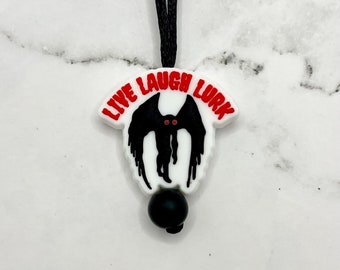 May include: White necklace with a black and white graphic of a creature with the text "Live Laugh Lurk" in red. The necklace has a black bead.