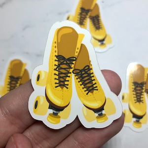 Op de afbeelding: Een paar gele rollerskates met zwarte veters. De skates hebben elk vier wielen en staan op een witte achtergrond.