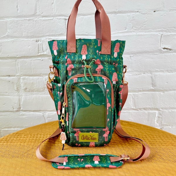 Könnte beinhalten: Grüne Tragetasche mit Pilzmuster, mit einer transparenten Vordertasche und braunen Trägern. Die Tasche hat einen abnehmbaren Schultergurt und einen kleinen Anhänger. Der Text "Artie Yan" ist auf der Vorderseite sichtbar.