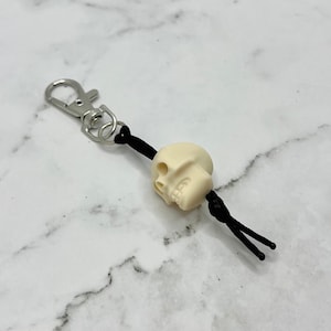 May include: A white skull keychain with a black cord and a silver metal clasp.