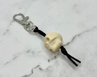 May include: A white skull keychain with a black cord and a silver metal clasp.