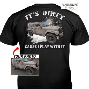 Op de afbeelding: Een zwart t-shirt met een afbeelding van een modderig terreinvoertuig. De tekst boven het voertuig luidt IT'S DIRTY en de tekst eronder luidt CAUSE I PLAY WITH IT. Een kleiner kader toont de originele foto van het gebruikte voertuig.