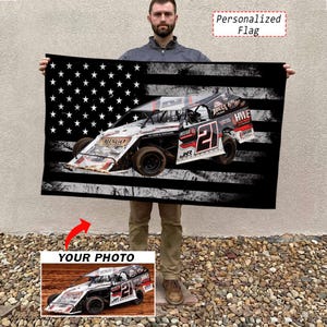 May include: A rectangular flag featuring a black and white distressed American flag pattern as a background. Centered on the flag is a graphic of a race car with the number 21, featuring red and black accents. The text Personalized Flag is visible.