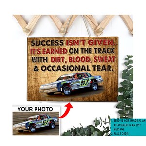 May include: Wooden sign with the text "SUCCESS ISN'T GIVEN. IT'S EARNED ON THE TRACK WITH DIRT, BLOOD, SWEAT & OCCASIONAL TEAR." A race car with the number 67 is featured on the sign. A smaller image of the car is below the sign.