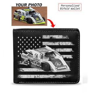 May include: A black bifold wallet featuring a white distressed American flag graphic overlaid with a detailed image of a number 35 dirt track race car. The wallet has visible white stitching along the edges and a rectangular shape.