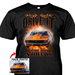 May include: Black t-shirt featuring an orange muscle car design with flames and the text "DRIVE IT LIKE YOU STOLE IT." A smaller image of the car is in the lower left corner.