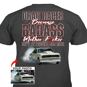 May include: Dark gray t-shirt with the text "DRAG RACER Because BADASS Mother F*cker ISN'T AN OFFICIAL JOB TITLE". A white race car is depicted below the text, with a smaller image of the car and the words "YOUR PHOTO" below it.