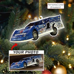 May include: A blue race car ornament featuring the number 1, Valvoline branding, and various sponsor logos. The ornament includes a gold hanging string and a rectangular inset displaying the text YOUR PHOTO above a matching race car image.