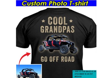 Puede incluir: Camiseta negra con un diseño de foto personalizado que presenta un vehículo todoterreno rojo y negro. El texto "*COOL* GRANDPAS GO OFF ROAD" está impreso en la camiseta.