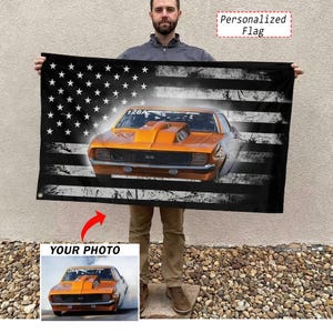 Könnte beinhalten: Eine schwarze Flagge mit einem verwitterten amerikanischen Flaggen-Design und einer orangefarbenen Muscle-Car-Grafik. Die Flagge trägt den Text "Personalized Flag" und "Your Photo". Das Auto hat die Nummer "128A" und "56".