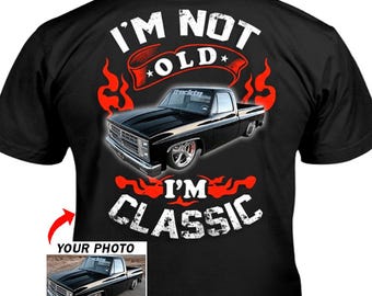 Puede incluir: Camiseta negra con un gráfico de una camioneta negra clásica. El texto "I'M NOT OLD, I'M CLASSIC" se muestra en blanco y rojo. Una imagen más pequeña de la camioneta está en la esquina inferior izquierda.