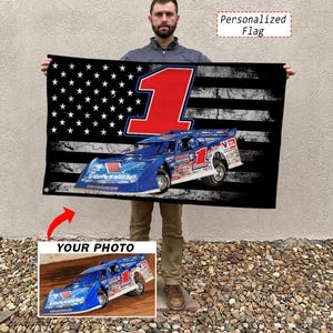May include: A rectangular flag featuring a distressed American flag pattern in black and white, a large red number one, and a blue race car with the Valvoline logo. The flag includes a smaller inset image showing the same blue race car on a dirt track.