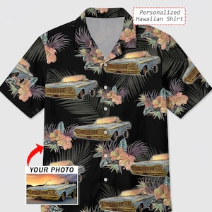 Puede incluir: Camisa hawaiana negra con un estampado repetido de coches clásicos azul claro, flores tropicales y hojas de palmera. La camisa tiene una botonadura y un cuello. El texto "Personalized Hawaiian Shirt" es visible.