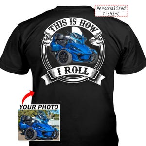 以下が含まれることがあります： 青い三輪オートバイのグラフィックが描かれた黒いTシャツ。デザインには円形のバナーの中に「THIS IS HOW I ROLL」というテキストが含まれています。小さな挿入ボックスには、同じ青いオートバイと、その上に「YOUR PHOTO」というテキストが表示されています。