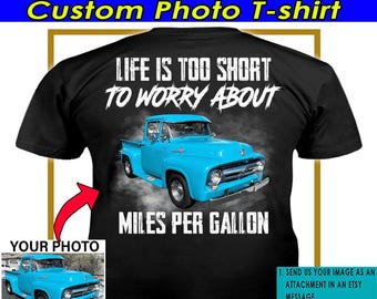 Puede incluir: Una camiseta negra con el texto "Life is too short to worry about miles per gallon" y una camioneta azul. El texto está en blanco y la camioneta está en el centro de la camiseta. Hay un espacio debajo de la camioneta para agregar una foto personalizada.