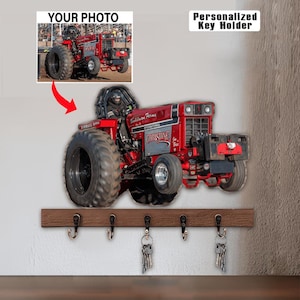 May include: A personalized key holder featuring a red tractor with black tires and the name "Christine." The key holder is mounted on a brown wooden plank with five metal hooks, each holding a set of keys. The text "Your Photo" and "Personalized Key Holder" are also visible.