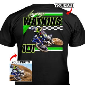 Peut inclure: Un t-shirt noir avec un motif représentant un pilote de motocross sur une moto bleue. Le design inclut le texte "LARRY WATKINS" et "101" en vert et blanc, un motif à damier et un encadré "YOUR PHOTO" avec une flèche rouge pointant dessus.