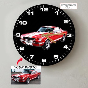 May include: A round wall clock with a black face featuring white numbers and gold hands. The center displays a red vintage car with white racing stripes. Below the clock, a small inset shows the same red car with the text YOUR PHOTO.