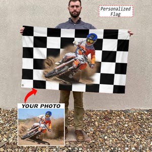 May include: A rectangular flag featuring a black and white checkered border pattern. The center displays a printed image of a motocross rider in orange and white gear on a dirt bike, kicking up dust. Text in the corner reads Personalized Flag.
