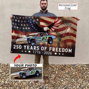 May include: A rectangular flag featuring a patriotic design with a bald eagle, the Statue of Liberty, and an American flag background. The text reads 250 YEARS OF FREEDOM 1776 - 2026. A race car with the number 67 is prominently displayed in the center.