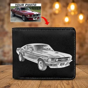 May include: A black leather bi-fold wallet featuring a white engraved illustration of a classic Ford Mustang fastback car with racing stripes on the hood. The wallet has visible white stitching along the edges and a rectangular shape.